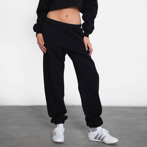 Person wearing a black cropped sweatshirt and black jogger pants with white sneakers on a plain background