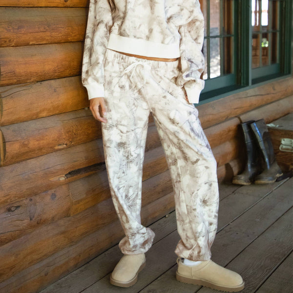 Woman in a white floral outfit standing in front of a wooden cabin.