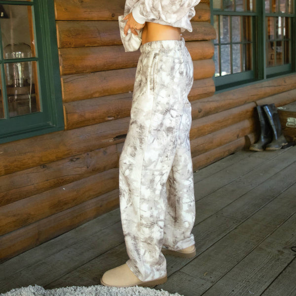 Woman in a patterned outfit standing on a wooden deck with a log cabin background